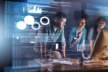 Shot of a group of programmers working together on a computer code at night.