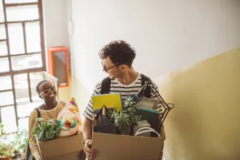 Young people moving in to apartment carying boxes.