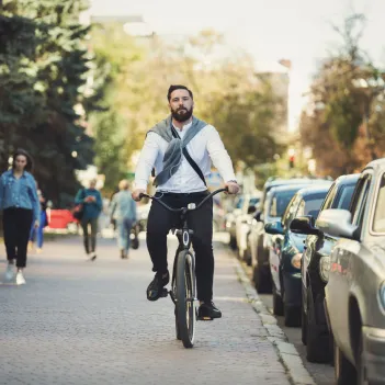 Young businessman going to work, riding bicycle on sidewalk in morning.