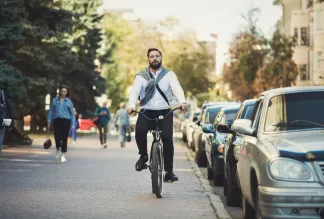 Young businessman going to work, riding bicycle on sidewalk in morning.