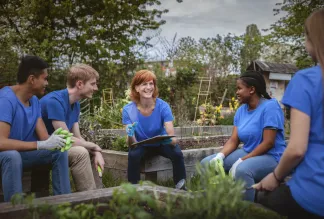 Female leader talks with group of younth volunteers gathered in community garden.