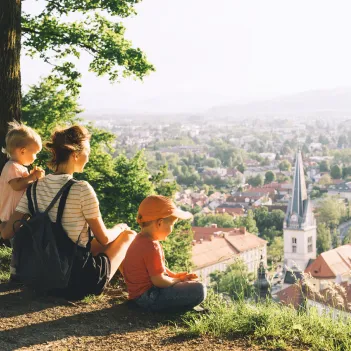 Woman with two little children looks at panorama of european city from a hill. 
